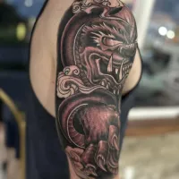 Ornamental black and grey dragon half sleeve wrapping the upper arm — by Adam Crane