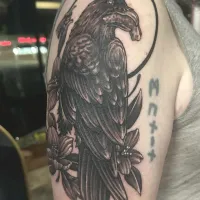 Black and grey raven perched below a full moon on an upper arm — by Adam Crane